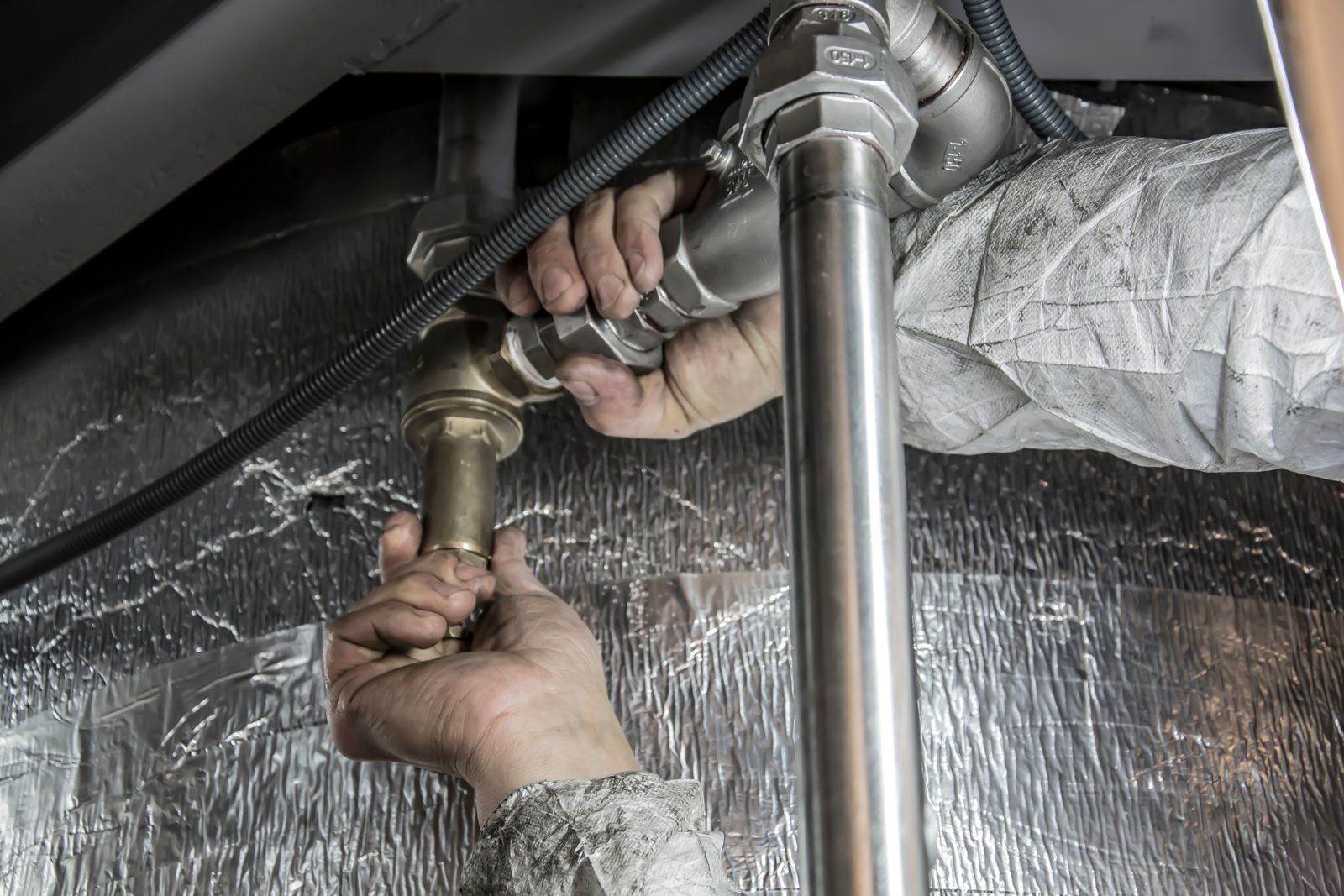 Plumber's hands tightening metal pipe fittings with a wrench